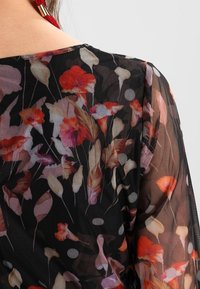 Průhledná černá látka s květinovým vzorem v odstínech červené, růžové a krémové, s puntíky a kulatým výstřihem na zádech.