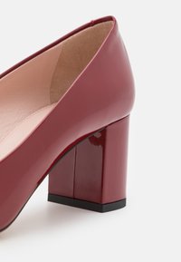 Chaussure à talon bloc pour femme, rouge foncé brillante, avec doublure intérieure beige et embout de semelle noir, vue de côté sur fond blanc.