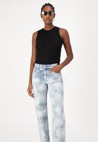 Top negro sin mangas y jeans de tono azul claro con un estampado de serpiente, que cuentan con un corte recto y un diseño de cinco bolsillos.