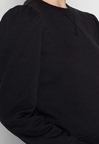 Svart sweatshirt med långa ärmar som har puffade axlar, rundad hals och en texturerad yta. Enkelt design utan mönster eller detaljer.