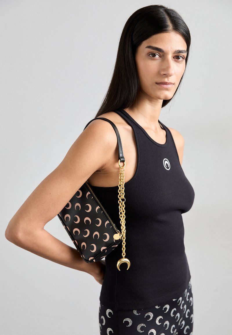 Top sin mangas negro de canalé con un logo circular, combinado con un bolso de mano negro que presenta patrones de luna creciente y una cadena dorada.