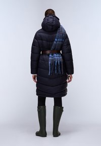 Piumino blu navy, con cintura in vita e cappuccio. Una sciarpa blu e grigia scende su una spalla. Stivali da pioggia verdi completano l'outfit.