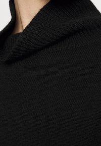 Black knitted sweater with a high, textured collar. The fabric has a soft, even knit pattern and a smooth, uniform appearance.
