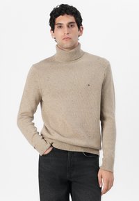 Beige garbó pulóver bordázott mandzsettákkal és alsó szegéllyel, amely finom pöttyös textúrával és egy kis logóval díszítve található a mellrészen.