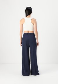 Top cropped branco com arestas, combinado com calças largas azul-marinho, com cintura alta, tecido suave e bolsos traseiros. Design minimalista.