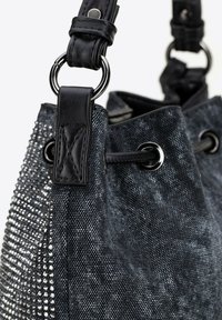 Zwarte denim emmer tas met een gestructureerd oppervlak, zilveren studs, leren accenten en een trekkoordsluiting met metalen oogjes.