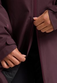 Parker-Jacke in tiefem Burgunderrot, mit einer glatten, wasserabweisenden Textur, durchgehendem Reißverschluss und verstellbaren Manschetten mit Klettverschluss.