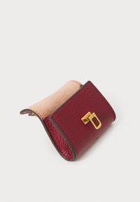 Burgundy leather wallet with gold hardware and a soft beige lining. Rounded rectangular shape, featuring a textured surface and no visible patterns.