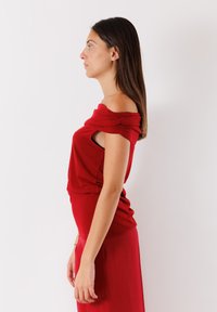 Abito rosso off-the-shoulder realizzato in tessuto morbido. Presenta dettagli arricciati alle spalle e una silhouette attillata che mette in risalto la vita.