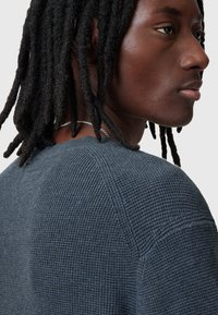 Pullover grigio scuro con texture a coste, scollatura rotonda e maniche corte, caratterizzato da un sottile dettaglio delle cuciture e una vestibilità rilassata.