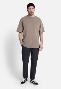 Beige oversized t-shirt med faldende skuldre, parret med mørkegrå tapered bukser og sorte sneakers med hvide snørebånd. Sort beanie bæres.