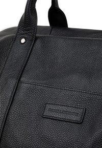 Czarna skórzana torba o teksturowanym wykończeniu, z solidnymi uchwytami oraz przednią naszywką z wytłoczonym logo. Srebrne akcenty metalowe.