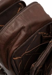 Intérieur d'un sac en cuir brun avec de multiples compartiments zippés, présentant une texture lisse et un doublure en tissu de marque de couleur marron foncé.