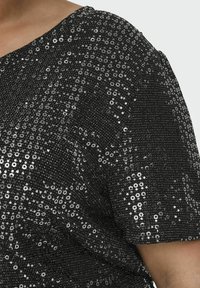 Top nero in tessuto texturizzato decorato con paillettes argentate, scollatura rotonda e maniche corte. La superficie riflette la luce.