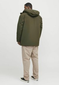 Olive green parka with a hood, made from smooth material; paired with light beige pants and black sneakers. Simple design with no visible logos.