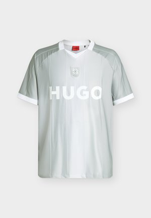 T-shirt de sport gris clair à manches courtes avec col blanc et bordures de manches blanches, rayures diagonales, emblème en forme de bouclier, et «HUGO» en lettres blanches épaisses au centre devant.