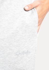 Pantalones jogger gris claro hechos de tela suave, con un bolsillo lateral y el logo bordado "Smiledex" en un azul sutil.