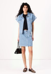 Jachetă din denim cu mâneci scurte și nasturi argintii, asociată cu o fustă din denim ajustată. Accesoriile includ o geantă mică de umăr neagră și balerini cu imprimeu animal.