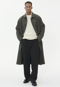 Cappotto a quadri grigio scuro, oversize, con colletto, indossato sopra un maglione di lana color crema e pantaloni neri. Scarpe nere con lacci completano l'outfit.