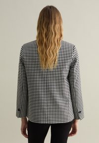 Blusa de cuadros vichy en blanco y negro con mangas largas, puños abotonados y corte recto. Tela de algodón suave; se muestra la vista trasera.