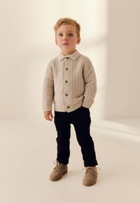 Beige knit cardigan with a collar and front buttons, paired with black pants and light brown suede shoes with laces. Simple and textured design.