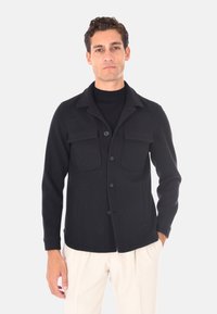 Giacca in mistura di lana nera con colletto, bottoni frontali, due tasche sul petto e tasche laterali; texture liscia, vestibilità sartoriale.