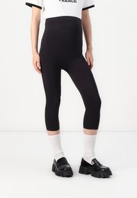 Leggings de maternidad negros con una cintura alta, longitud cropped, tejido elástico, textura suave y silueta ajustada. Llevados con mocasines negros y calcetines blancos.