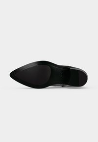 Semelle d'une chaussure de ville noire à bout pointu avec des zones d'adhérence en caoutchouc lisses et texturées sur un fond clair uni.