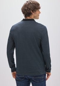 Marineblaues Langarm-Poloshirt mit strukturiertem Muster und schwarzem Kragen. Der Stoff scheint weich zu sein, tailliert und hat einen geraden Saum.