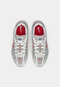 Ein Paar graue und weiße Nike-Laufschuhe mit roten Akzenten, weißen Schnürsenkeln und roten Innensohlen, die das Nike-Swoosh-Logo tragen, von oben gesehen.