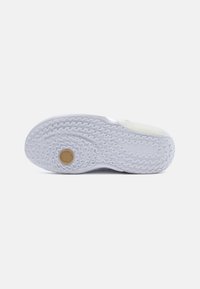 White sneaker sole with a textured design, featuring a circular gold emblem and raised zigzag patterns for traction.