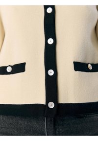 Krämfärgad cardigan med svarta detaljer, prydd med fem vita knappar och två framfickor, tillverkad av ett mjukt tyg med en slät yta.