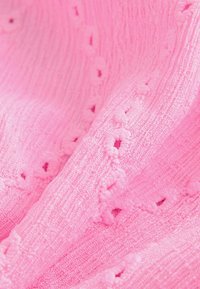 Tissu tricoté rose doux avec de petites trous décoratifs et des motifs texturés créant un design délicat et complexe.