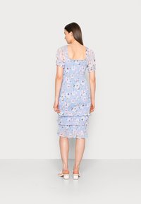 Vestido floral em azul claro com mangas bufantes, camadas franzidas na bainha e costas em forma de quadrado. Tecido macio e texturizado com padrões florais coloridos.