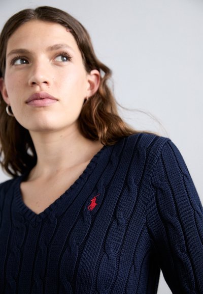 Navy cable-knit sweater with a V-neck and a small red logo on the chest. Features ribbed edges and a textured fabric.