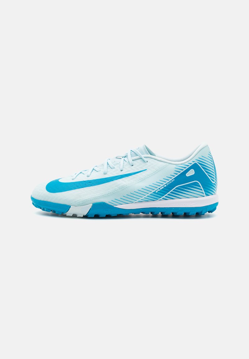 Zapatilla deportiva Nike blanca y azul de perfil bajo con suela texturizada y gran logo de swoosh, mostrada en vista lateral sobre un fondo blanco.