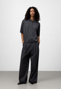 Polo shirt grigio scuro con un fit rilassato e maniche corte, caratterizzato da una patta con due bottoni. Abbinato a pantaloni grigi a gamba larga e scarpe appuntite.