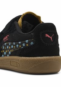Czarne zamszowe sneakersy z wzorzystym bokiem, na którym znajdują się niebieskie i żółte kropki, gumową podeszwą oraz różowymi logo Pumy na pięcie i boku.