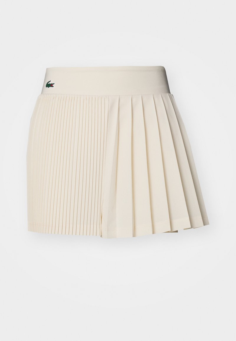 Short en beige plissé avec une finition texturée, présentant une taille solide et un petit logo de marque en vert.