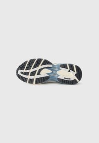 Black rubber outsole with deep grooves and white accents, featuring a textured blue midsole and Reebok branding.