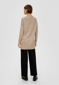 Lange beige sweater met een geribbelde zoom, met een relaxte pasvorm en zijsplitten. Gecombineerd met zwarte wijde broek en chunky zwarte schoenen.