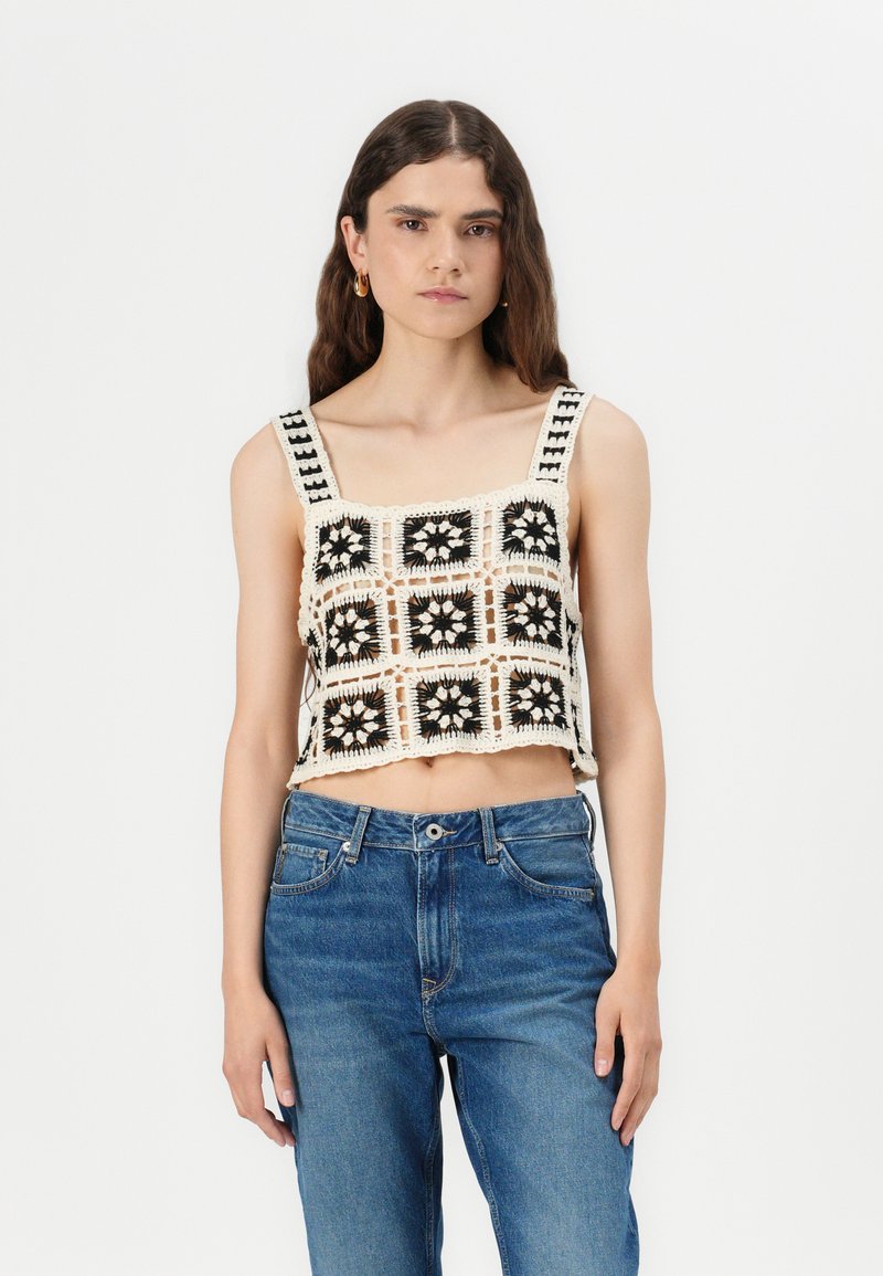 Top corto de ganchillo con escote cuadrado, adornado con patrones geométricos en blanco y negro, combinado con unos pantalones vaqueros de cintura alta en azul.