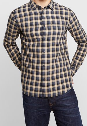 Camisa de cuadros de manga larga en beige y azul marino, con cuello abotonado, dos bolsillos en el pecho y un dobladillo redondeado. Fabricada en tejido tejido.