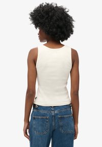 Hvid ribbet tanktop med rund halsudskæring og slim fit, parret med slidte blå denim jeans med baglommer.
