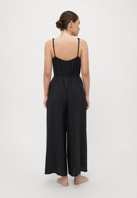 Mono negro con tirantes finos ajustables, cuerpo ajustado y silueta de pierna ancha. Tela suave con un diseño limpio y minimalista.