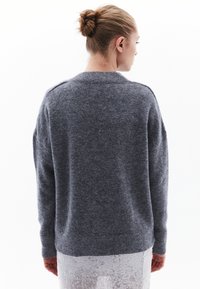 Szary sweter z dzianiny z okrągłym dekoltem, obniżonymi ramionami oraz ściągaczami na mankietach i dole. Miękka faktura i luźny krój.