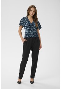 Krátký rukáv, černá a modrozelená vzorovaná blůza se shromážděným předním dílem, kombinovaná s černými zužujícími se kalhotami a černými lodičkami se špičkou.