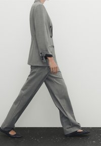 Grijze op maat gemaakte blazer met dubbele rij knopen, gecombineerd met bijpassende wijde broek en zwarte platte schoenen. Gladde stof, minimale patronen.