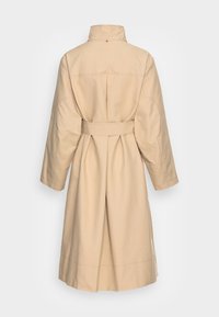 Trench long beige avec une large ceinture, une fente arrière et des détails cousus dans le dos et sur les manches, présenté de dos sur fond blanc.