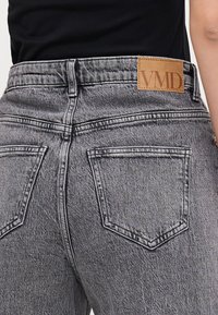 Pilki džinsai su aukštu juosmeniu, su odiniu etikete, pažymėta "VMD". Audinys turi tekstūruotą paviršių ir tradicinius užpakalinius kišenes.